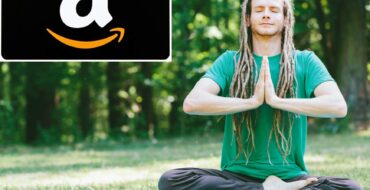 A young white man with long dreadlocks in a green t-shirt and black sweatpants sits crosslegged on a mat in a meadow in front of a forested area, meditating with his eyes closed and his hands pressed together in front of his chest in a prayer pose. In the top left corner of the image, there's an insert of a $25 Amazon gift card.