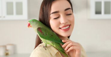 a woman with a green bird on her shoulder who she's stroking lovingly