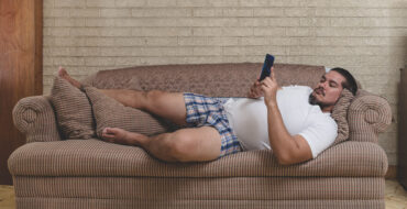 A typical couch potato - A man in his underwear laying on the sofa and watching videos, playing mobile games or on social media.