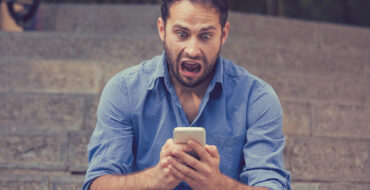 a man sitting on some steps outside is looking at his phone in horror