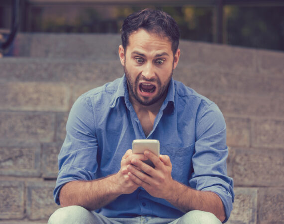 a man sitting on some steps outside is looking at his phone in horror