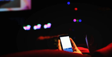 A pair of hands in a dark movie theatre are holding a very bright phone