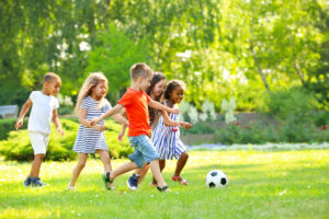 a group of five young children playing soccer on a green lawn on a beautiful day