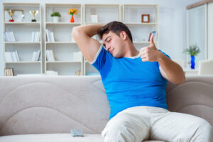 A man is sitting down, smelling his own sweaty armpit and giving a thumbs up