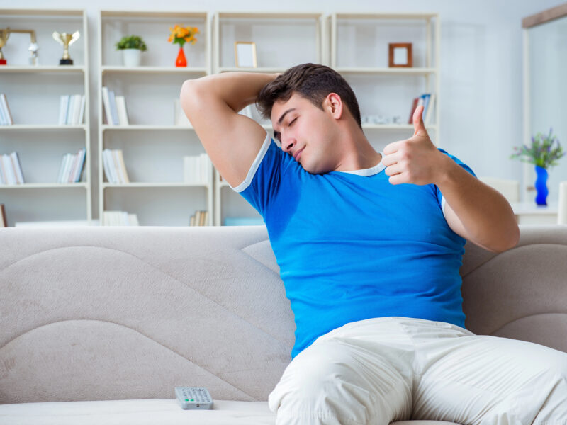 A man is sitting down, smelling his own sweaty armpit and giving a thumbs up