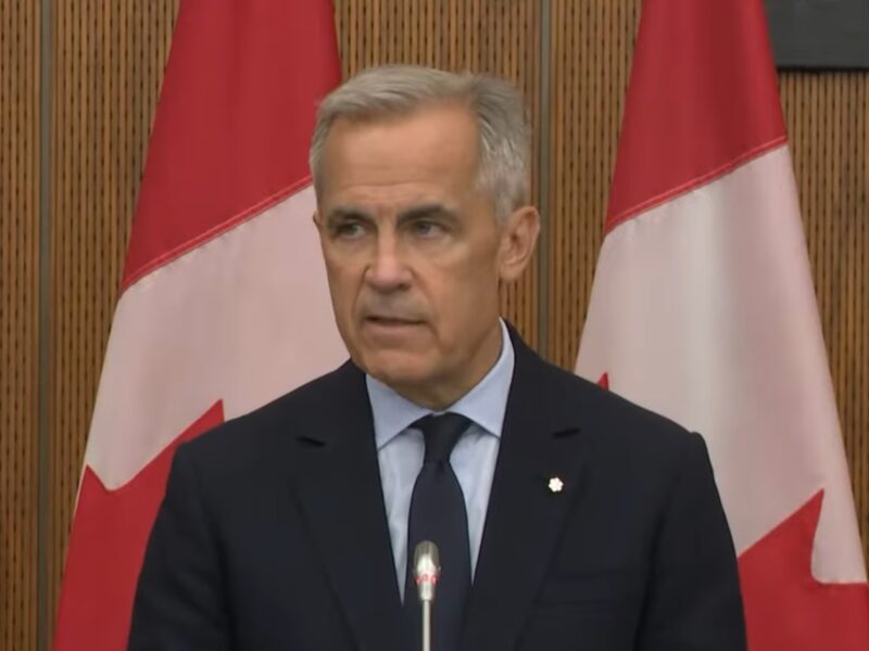 Mark Carney giving a speech in front of Canadian flags
