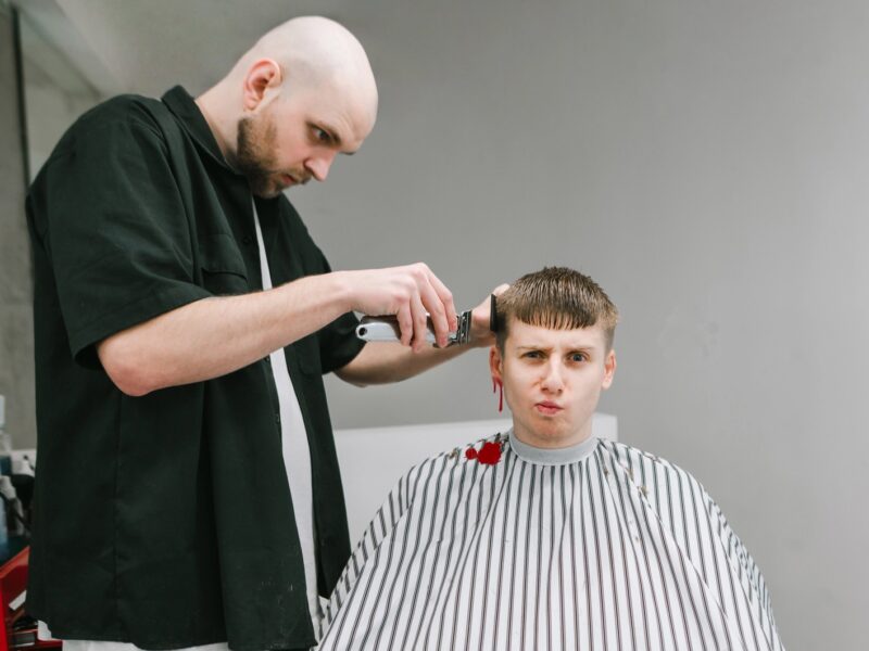 A man getting a haircut with an unhappy expression on his face while his right ear bleeds