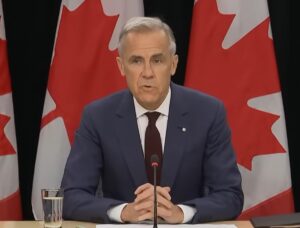 Mark Carney sitting at a desk in front of several Canadian flags